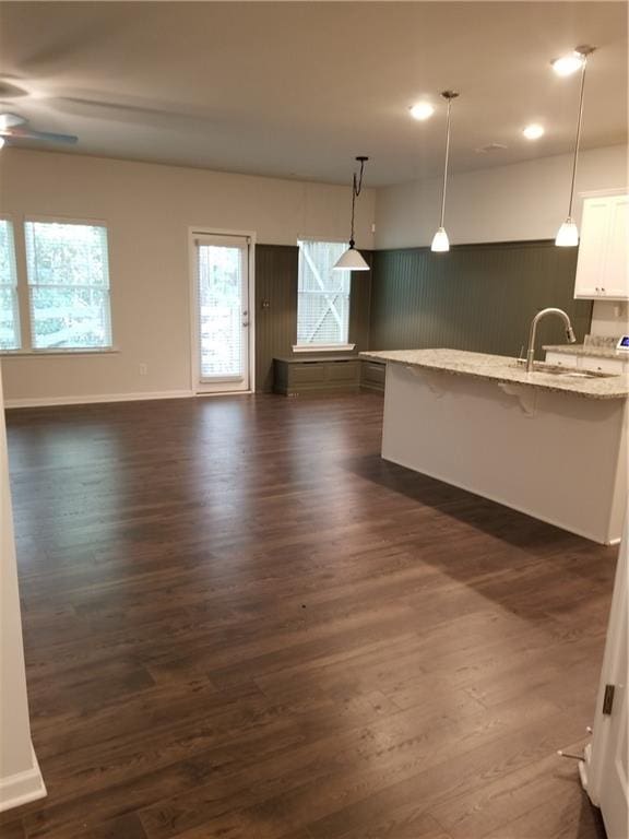 kitchen with hanging light fixtures, a breakfast bar, light stone countertops, white cabinetry, and dark hardwood / wood-style flooring