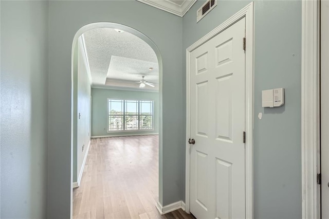 hall with crown molding, light wood-type flooring, and a textured ceiling