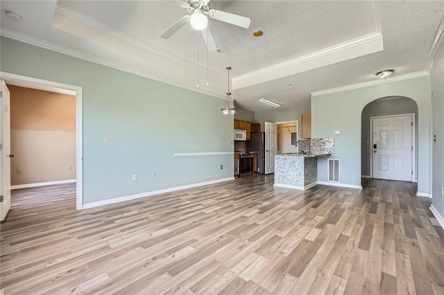 unfurnished living room with ceiling fan, a tray ceiling, ornamental molding, light hardwood / wood-style floors, and a textured ceiling