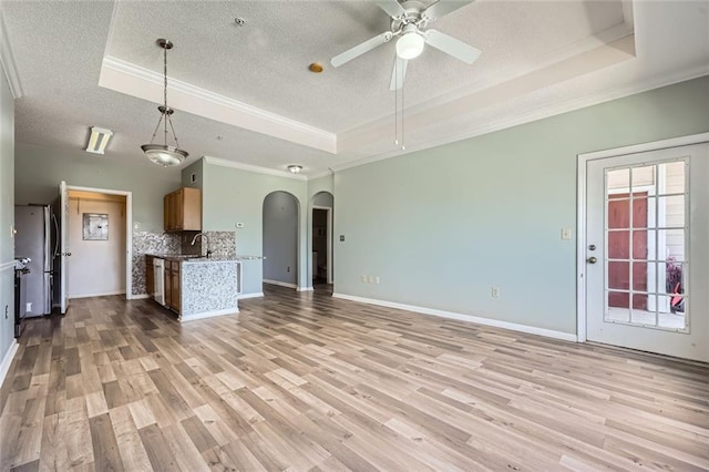 unfurnished living room with sink, a tray ceiling, and light wood-type flooring