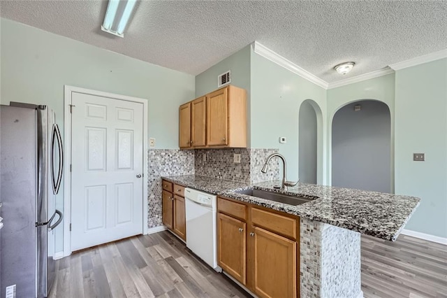 kitchen with sink, hardwood / wood-style flooring, stainless steel refrigerator, white dishwasher, and kitchen peninsula