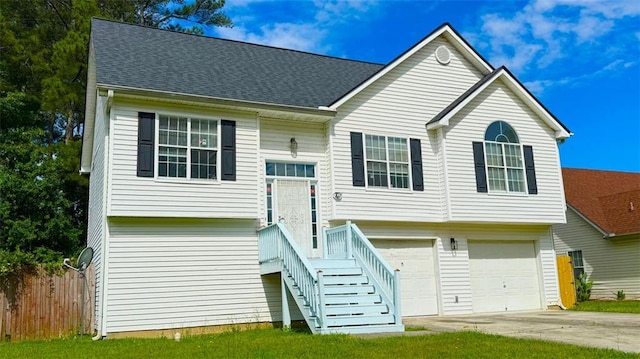bi-level home with an attached garage, concrete driveway, fence, and roof with shingles
