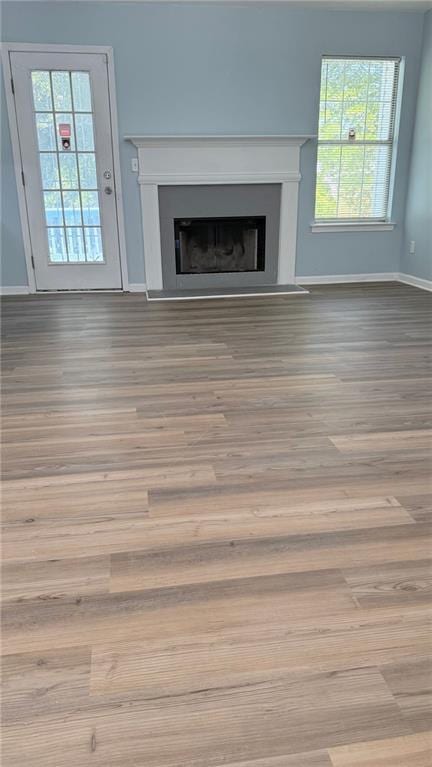 unfurnished living room with wood finished floors, baseboards, a fireplace, and plenty of natural light