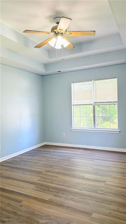 spare room with a raised ceiling, baseboards, wood finished floors, and a ceiling fan