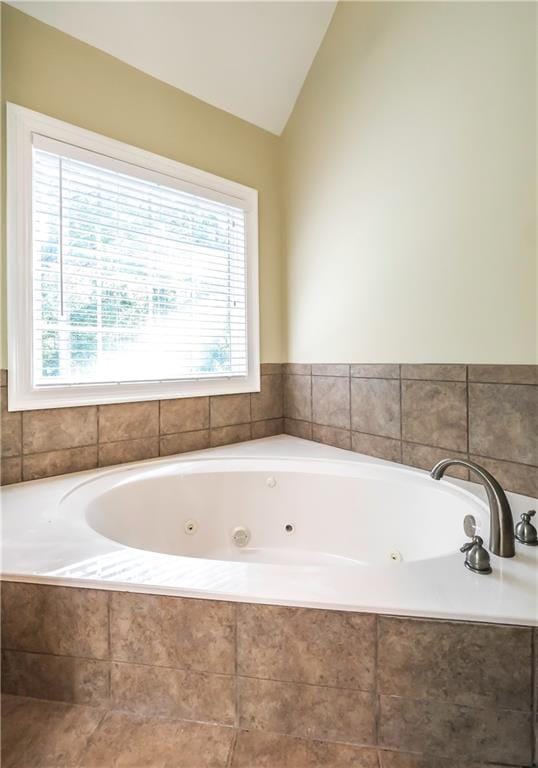 bathroom featuring tiled tub, plenty of natural light, and vaulted ceiling