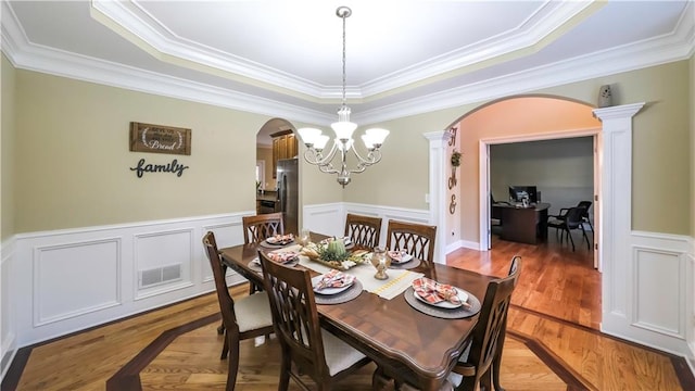 dining room with wood-type flooring, decorative columns, a tray ceiling, a notable chandelier, and ornamental molding