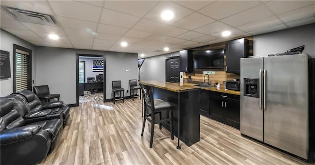 bar featuring stainless steel refrigerator with ice dispenser, sink, light stone counters, a paneled ceiling, and light hardwood / wood-style floors