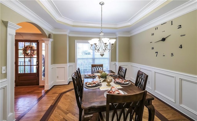 dining space with crown molding, ornate columns, wood-type flooring, and a raised ceiling