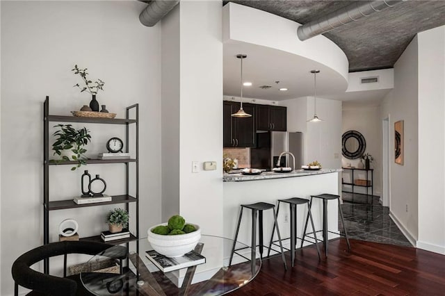 kitchen featuring visible vents, dark wood-type flooring, a breakfast bar area, decorative backsplash, and stainless steel refrigerator with ice dispenser