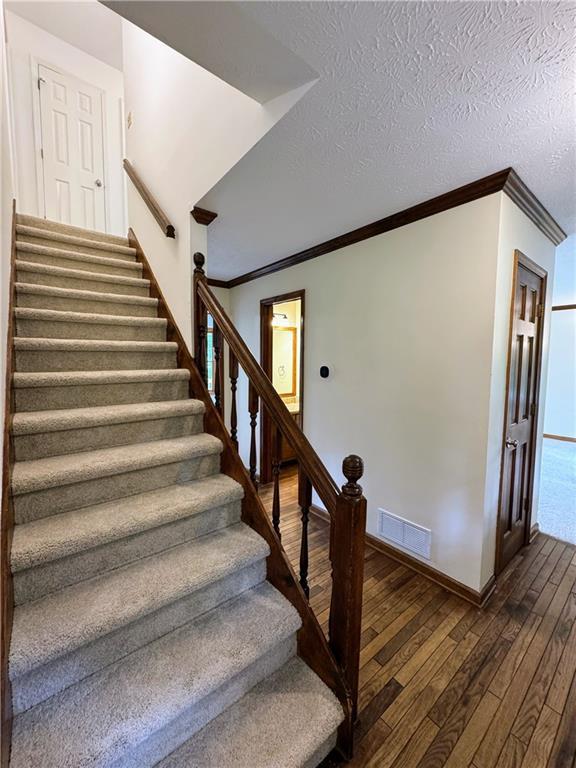 stairway with wood-type flooring, crown molding, and baseboards