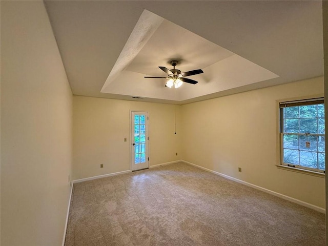 carpeted empty room with a raised ceiling, baseboards, and ceiling fan
