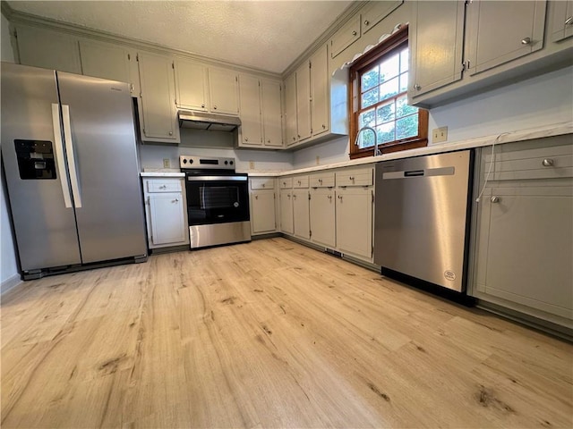 kitchen with appliances with stainless steel finishes, under cabinet range hood, gray cabinetry, light wood-style flooring, and light countertops