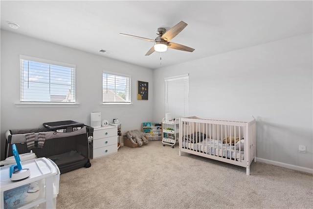 carpeted bedroom featuring a crib and ceiling fan