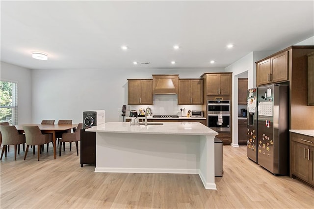 kitchen featuring stainless steel appliances, light hardwood / wood-style floors, a center island with sink, and light stone counters