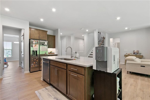 kitchen with light hardwood / wood-style floors, stainless steel appliances, a center island with sink, sink, and light stone countertops