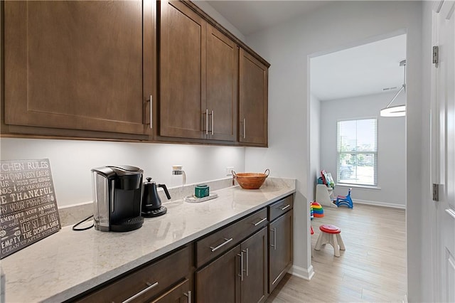 kitchen featuring dark brown cabinets, light hardwood / wood-style floors, and light stone counters