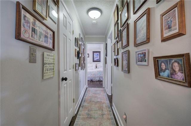 hall with a textured ceiling, crown molding, and baseboards