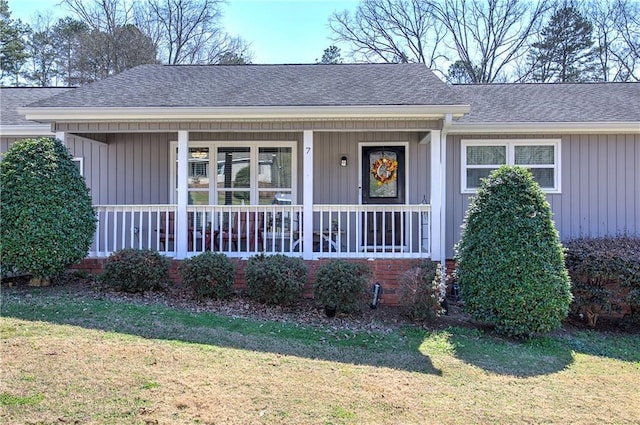 view of front of property with board and batten siding, a front yard, covered porch, and roof with shingles