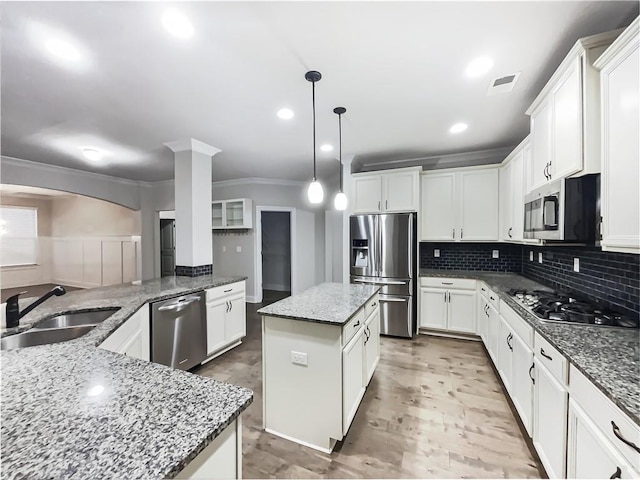 kitchen featuring sink, hanging light fixtures, stainless steel appliances, light stone counters, and a kitchen island