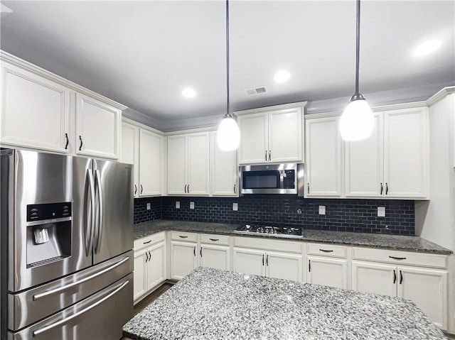 kitchen with appliances with stainless steel finishes, decorative light fixtures, dark stone countertops, white cabinets, and backsplash