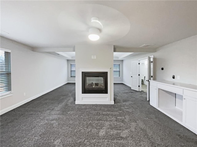 unfurnished living room featuring a multi sided fireplace and dark colored carpet