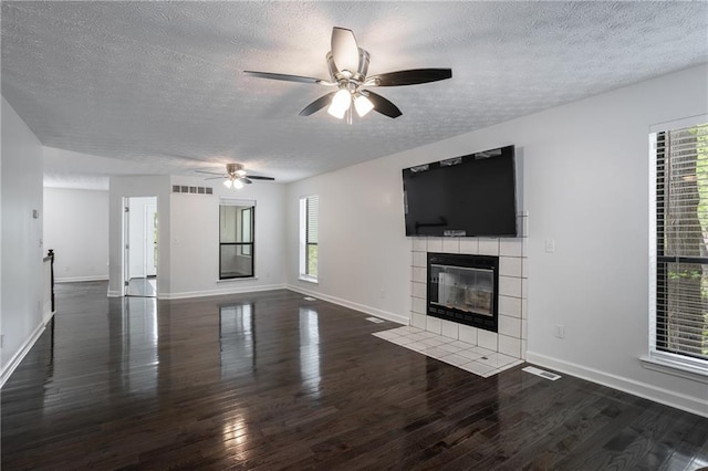 unfurnished living room featuring a tile fireplace, ceiling fan, dark wood-type flooring, and a textured ceiling