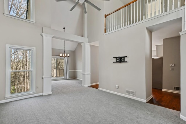 unfurnished living room with high vaulted ceiling, ceiling fan with notable chandelier, ornate columns, and carpet flooring