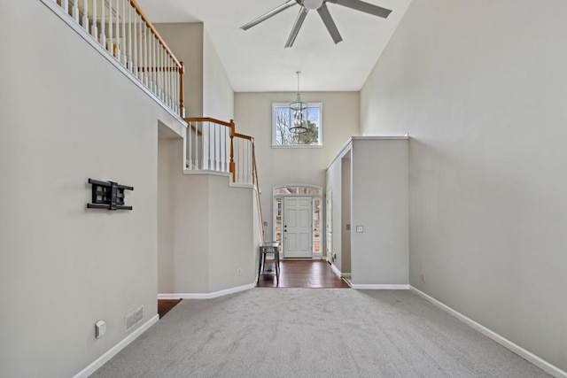 carpeted foyer with ceiling fan with notable chandelier and a high ceiling