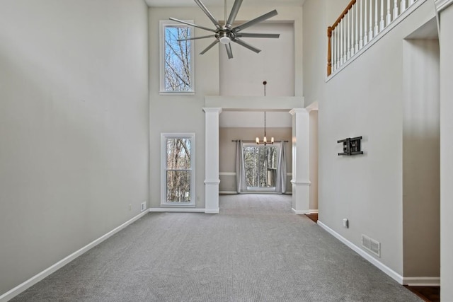 unfurnished living room with ornate columns, ceiling fan with notable chandelier, a high ceiling, and carpet floors