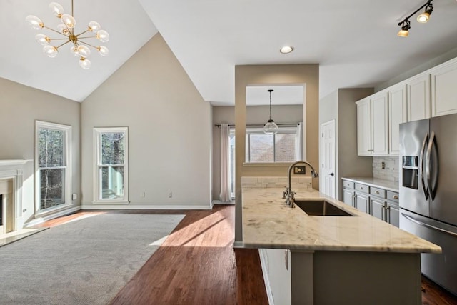 kitchen featuring decorative light fixtures, stainless steel refrigerator with ice dispenser, sink, and light stone counters