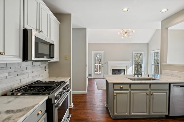 kitchen featuring white cabinetry, appliances with stainless steel finishes, lofted ceiling, light stone countertops, and sink