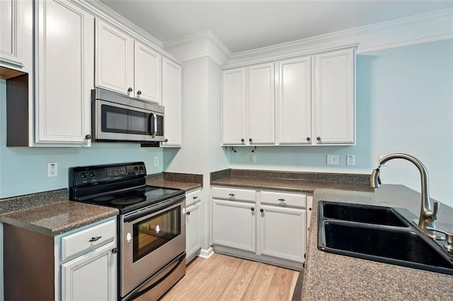kitchen featuring light wood finished floors, a sink, white cabinets, crown molding, and appliances with stainless steel finishes