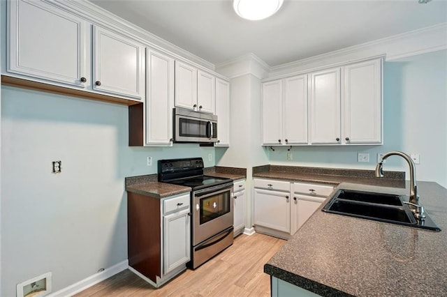 kitchen featuring a sink, dark countertops, stainless steel appliances, white cabinets, and light wood-style floors
