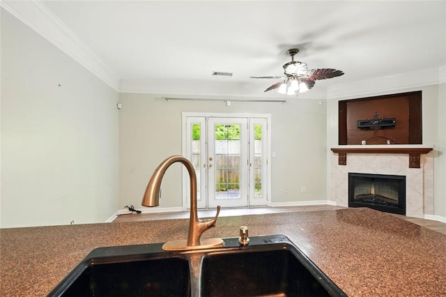 kitchen featuring a tile fireplace, crown molding, ceiling fan, and a sink