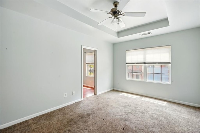 unfurnished room featuring visible vents, carpet flooring, a ceiling fan, a raised ceiling, and baseboards