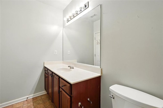 bathroom with toilet, vanity, stone finish floor, visible vents, and baseboards