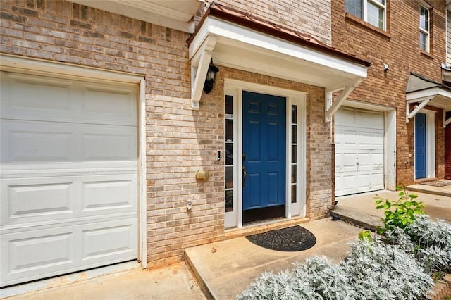 view of exterior entry with a garage and brick siding