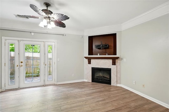 unfurnished living room featuring wood finished floors, a tiled fireplace, crown molding, baseboards, and ceiling fan