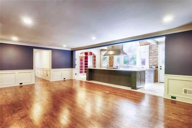 unfurnished living room featuring a decorative wall, crown molding, a wainscoted wall, light wood finished floors, and a sink