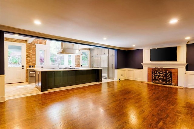 unfurnished living room with a decorative wall, crown molding, light wood-type flooring, a wainscoted wall, and a brick fireplace