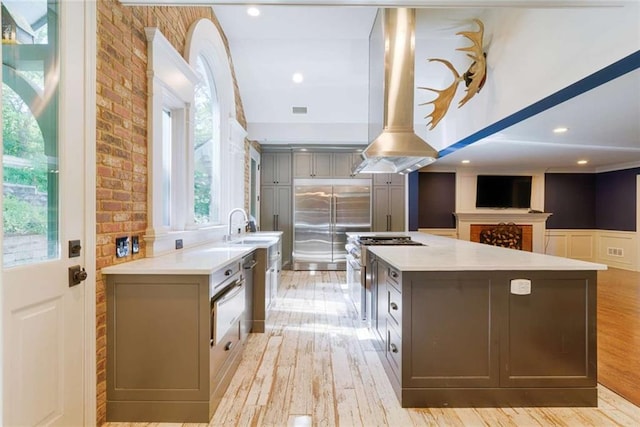 kitchen with light countertops, gray cabinetry, light wood finished floors, a sink, and high end appliances