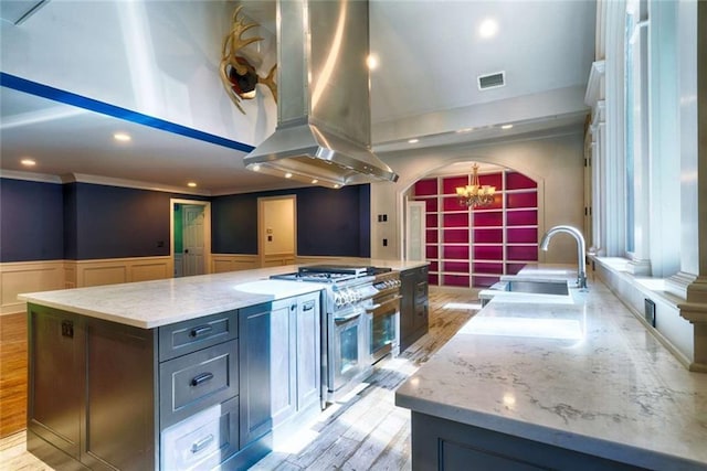 kitchen with a sink, a chandelier, range with two ovens, island exhaust hood, and a decorative wall