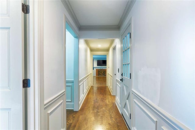 corridor with crown molding, a decorative wall, dark wood-style flooring, and a wainscoted wall