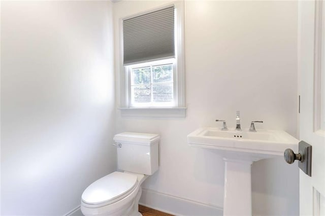 half bath with baseboards, toilet, and a sink