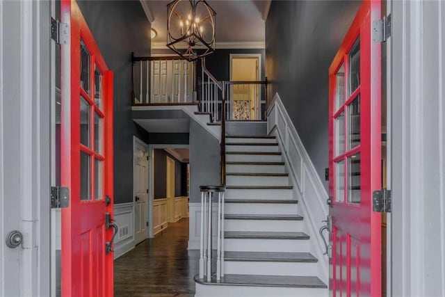 foyer entrance featuring stairs, a chandelier, a high ceiling, a wainscoted wall, and ornamental molding