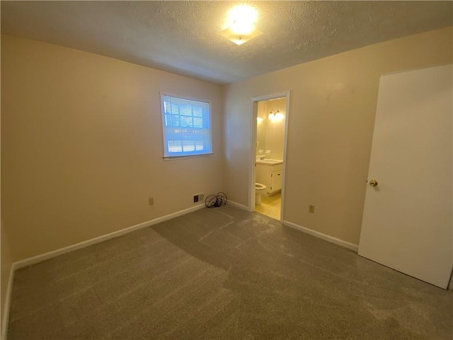 unfurnished bedroom with ensuite bath, sink, dark carpet, and a textured ceiling