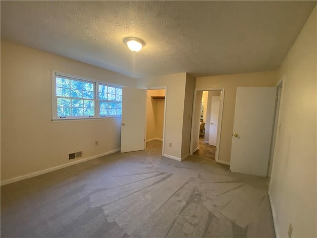 unfurnished bedroom featuring carpet flooring, a walk in closet, a textured ceiling, and a closet