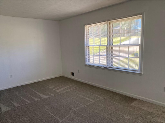 spare room featuring dark carpet and a wealth of natural light