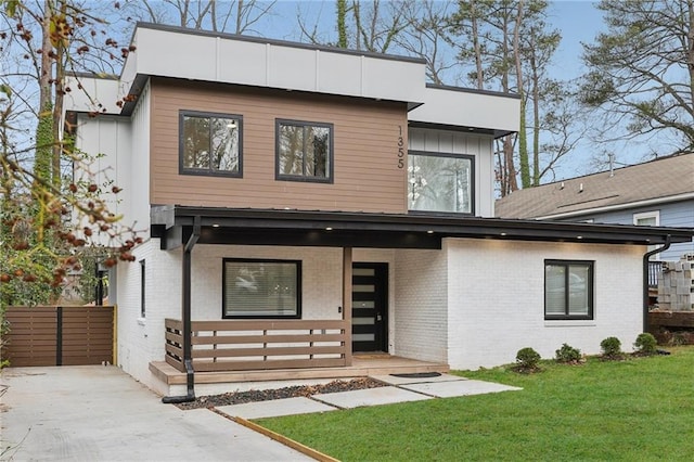 contemporary house featuring brick siding, board and batten siding, a porch, and a front yard