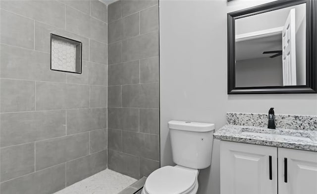 full bathroom featuring toilet, a tile shower, and vanity